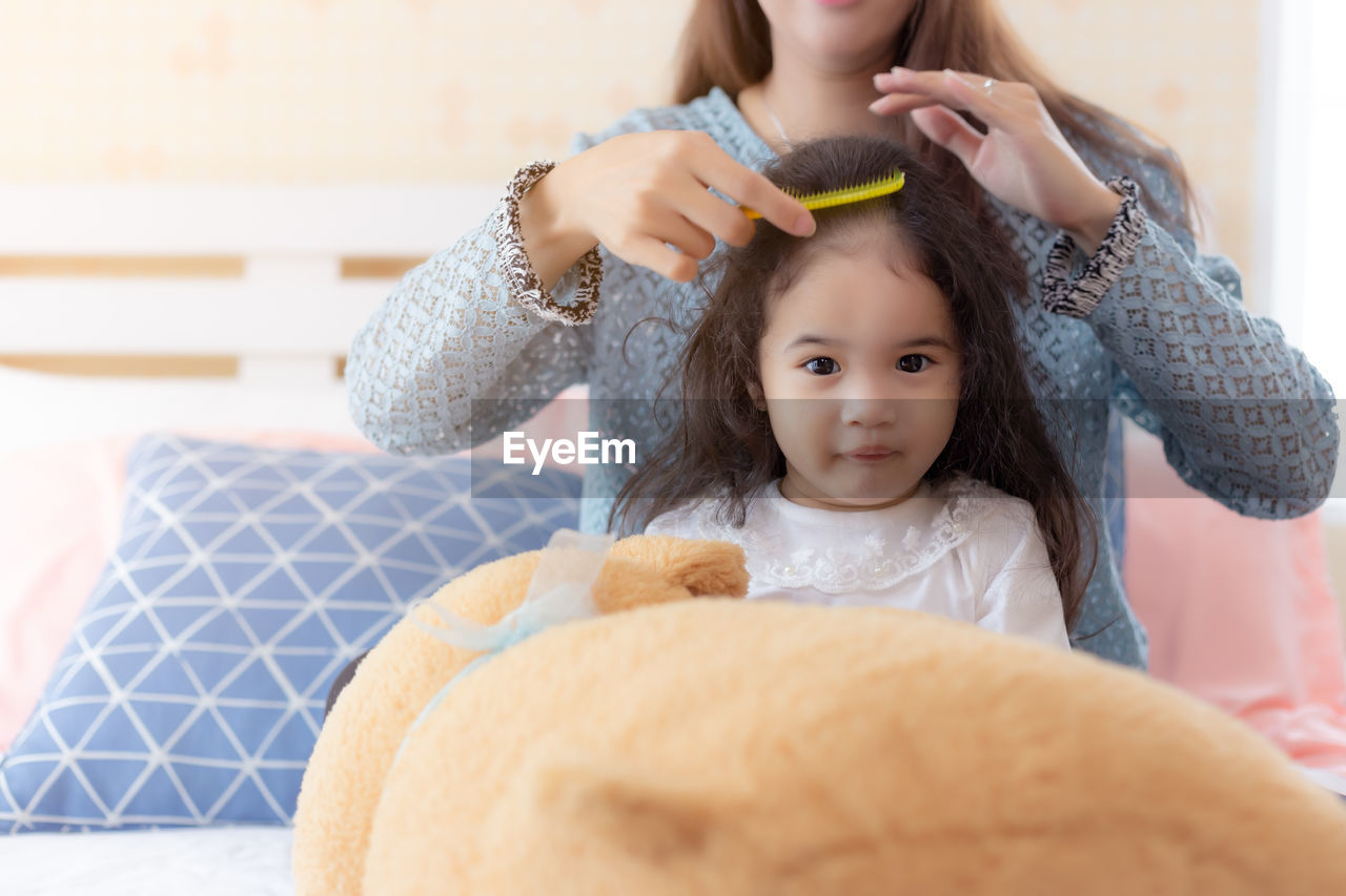 Midsection of mother combing daughter hair at home