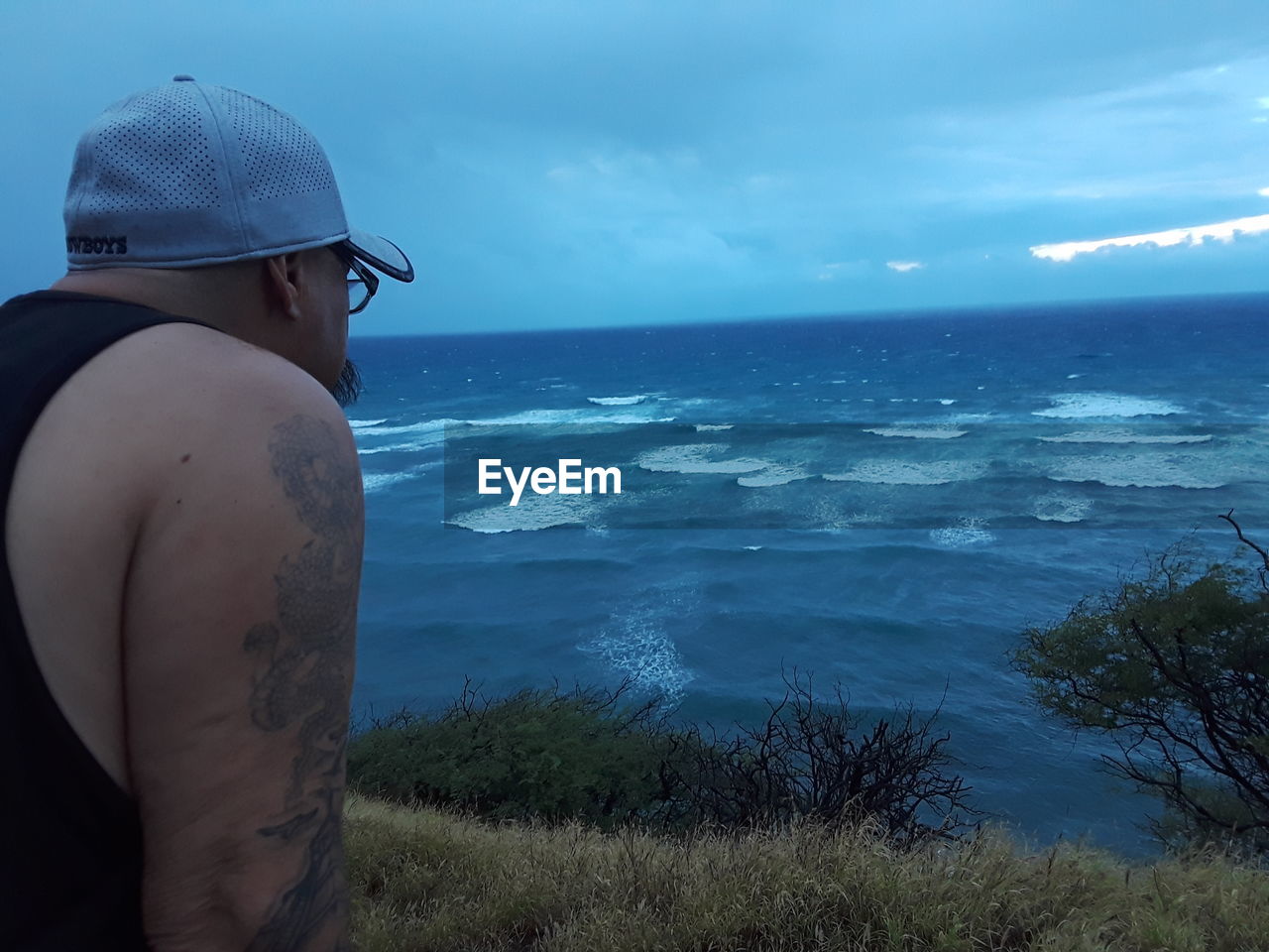 MAN STANDING BY SEA AGAINST SKY DURING SUNSET