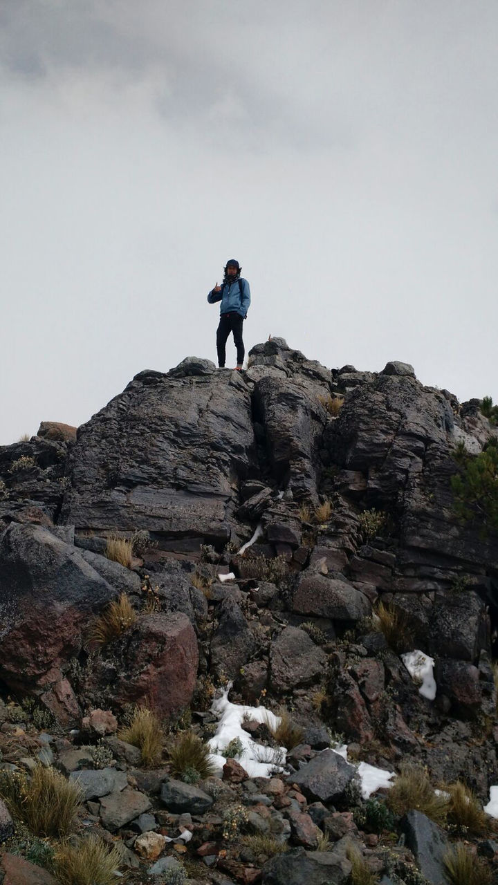 Low angle view of man standing on cliff against sky