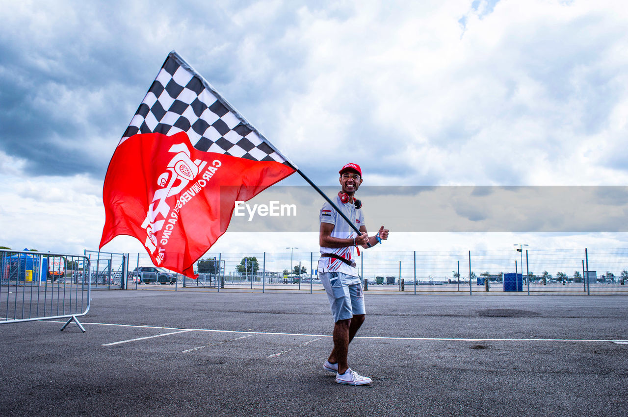 WOMAN STANDING BY FLAG AGAINST SKY