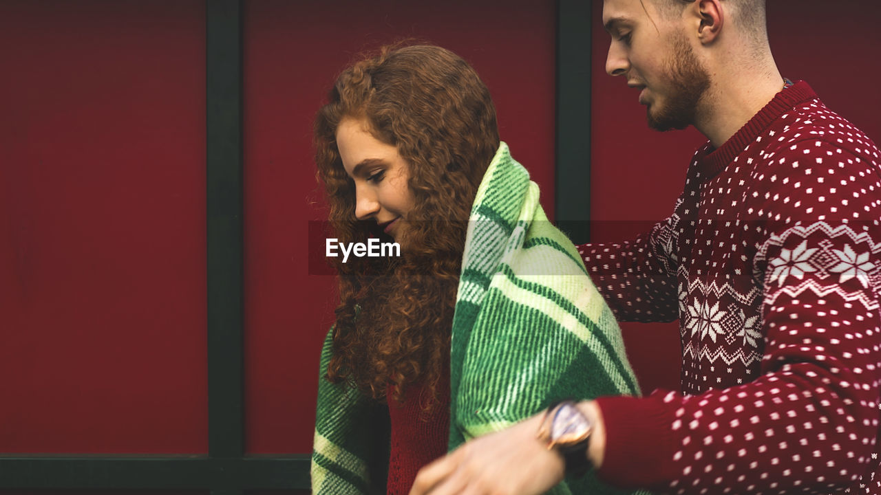 Beautiful young guy and girl cuddling in a green plaid and christmas colors on a red background.