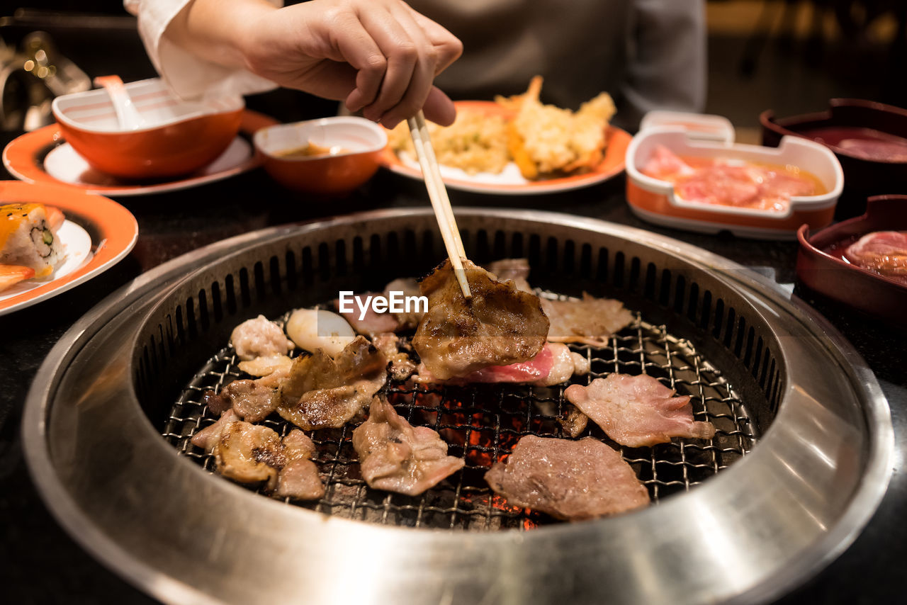 Midsection of woman using chopsticks while picking food from metal grate