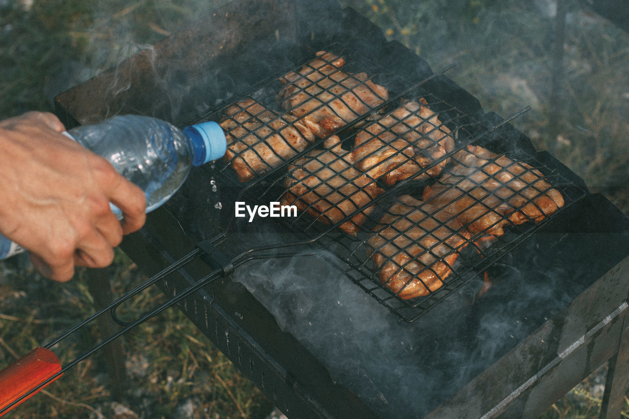 Cropped hand of person pouring water on barbecue grill