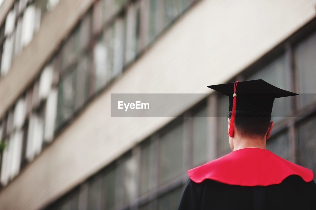 Rear view of man wearing graduation gown against building