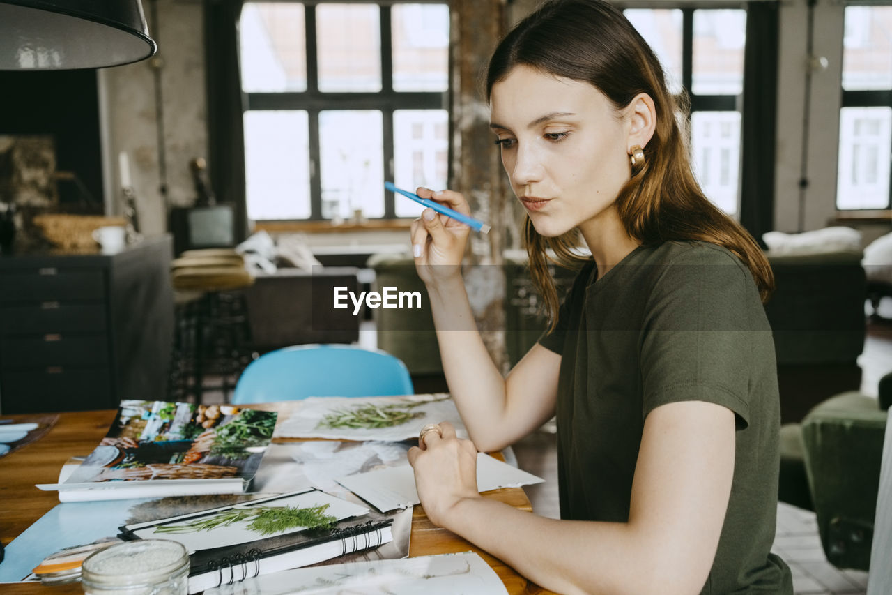 Thoughtful female food stylist puckering lips and holding pen while working in studio