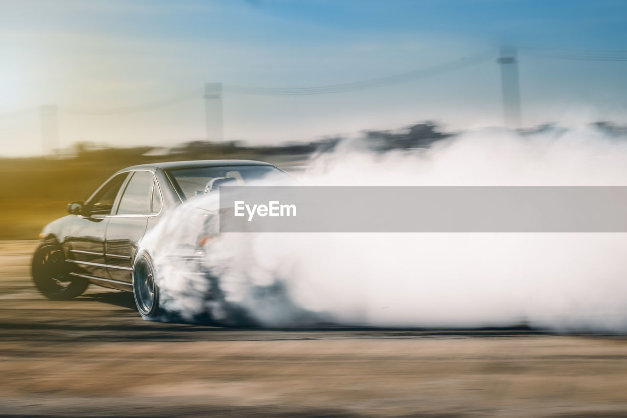 Blurred motion of car emitting smoke against sky