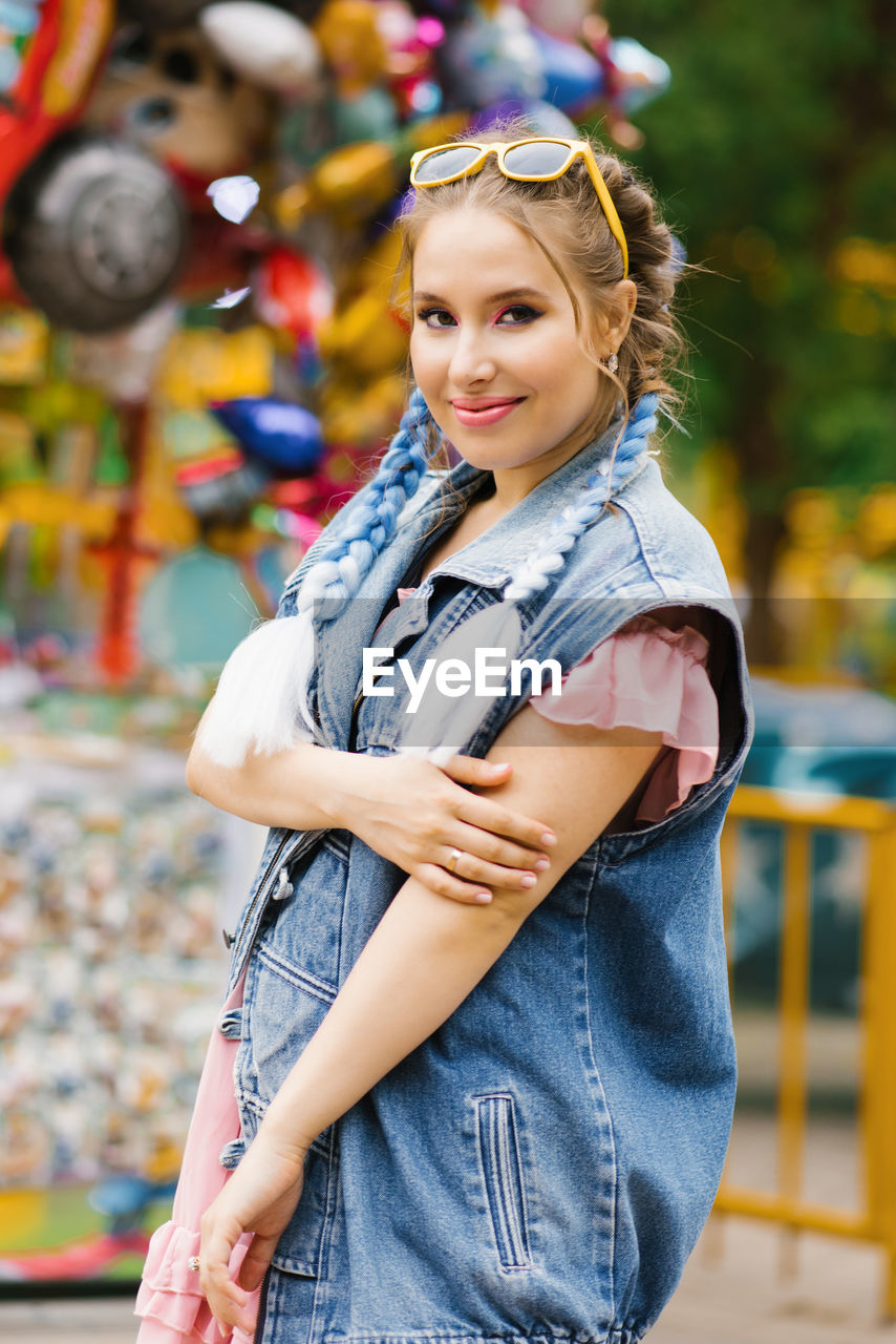 Young woman with blue pigtails in a denim vest in an amusement park