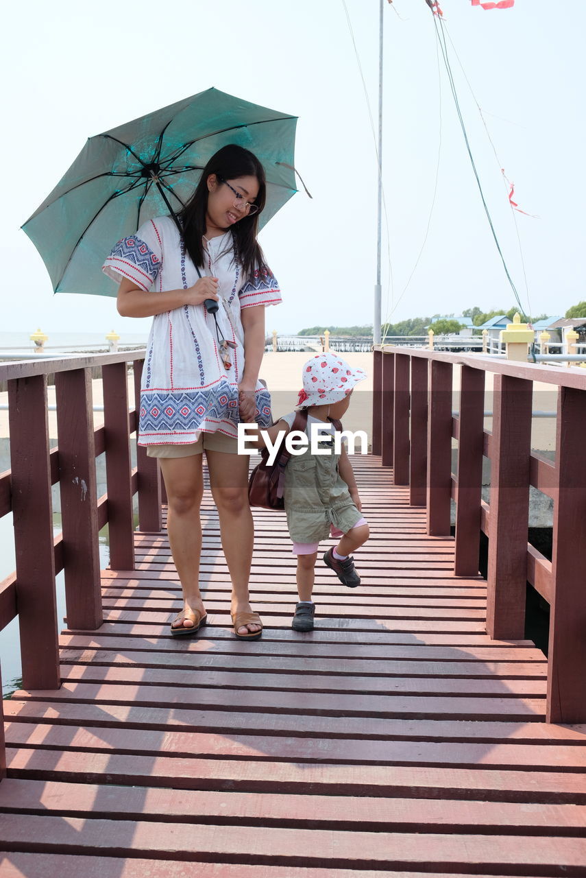 Full length of mother and daughter standing on pier against sky