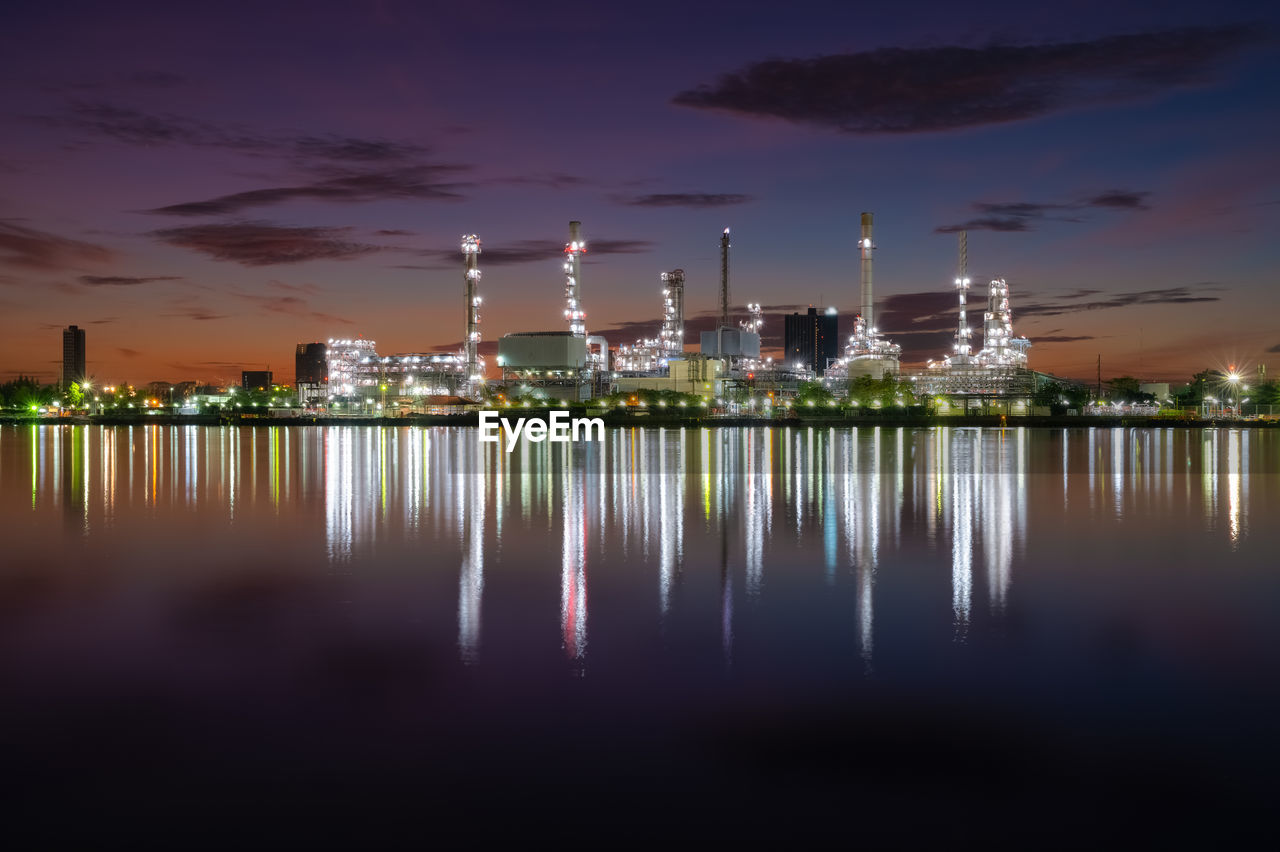 ILLUMINATED FACTORY BY RIVER AGAINST SKY