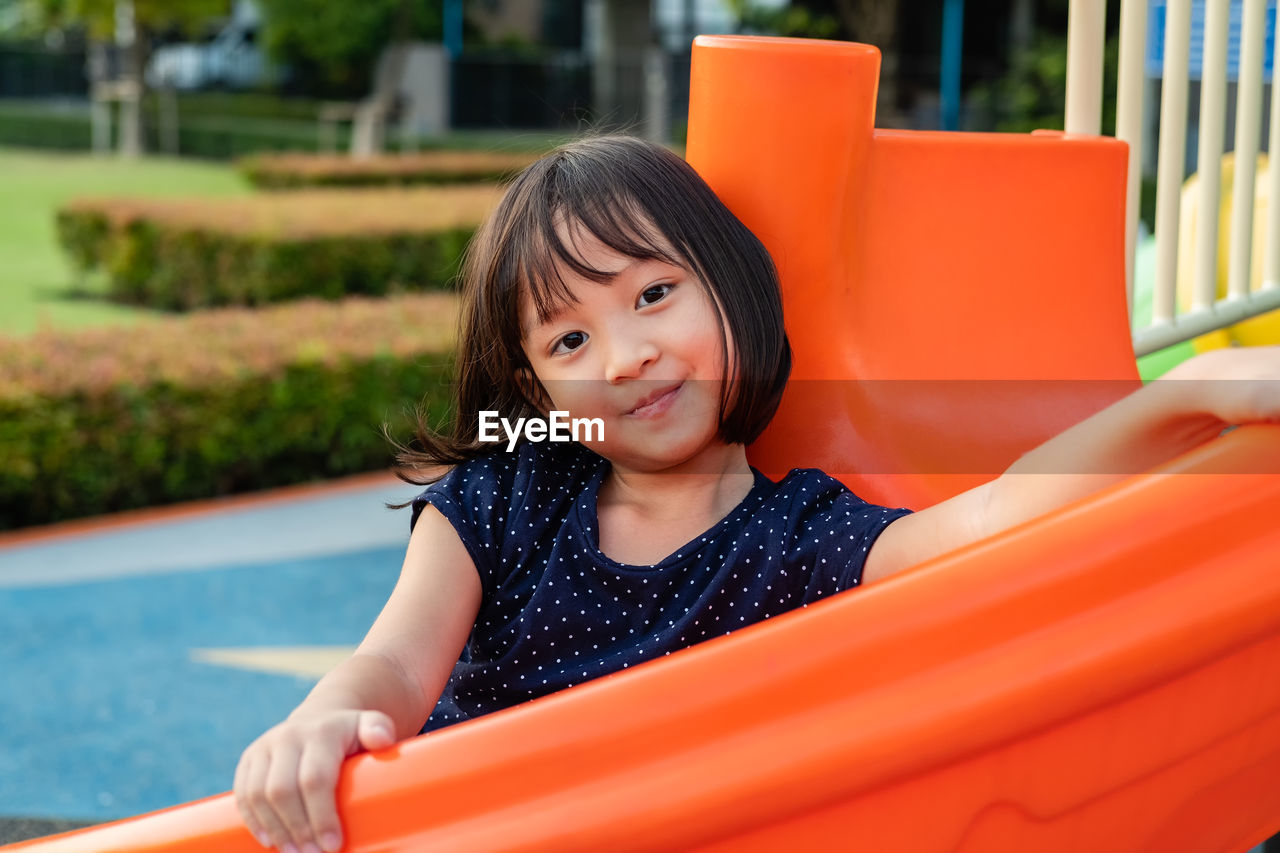 Portrait of smiling girl sitting on slide in playground