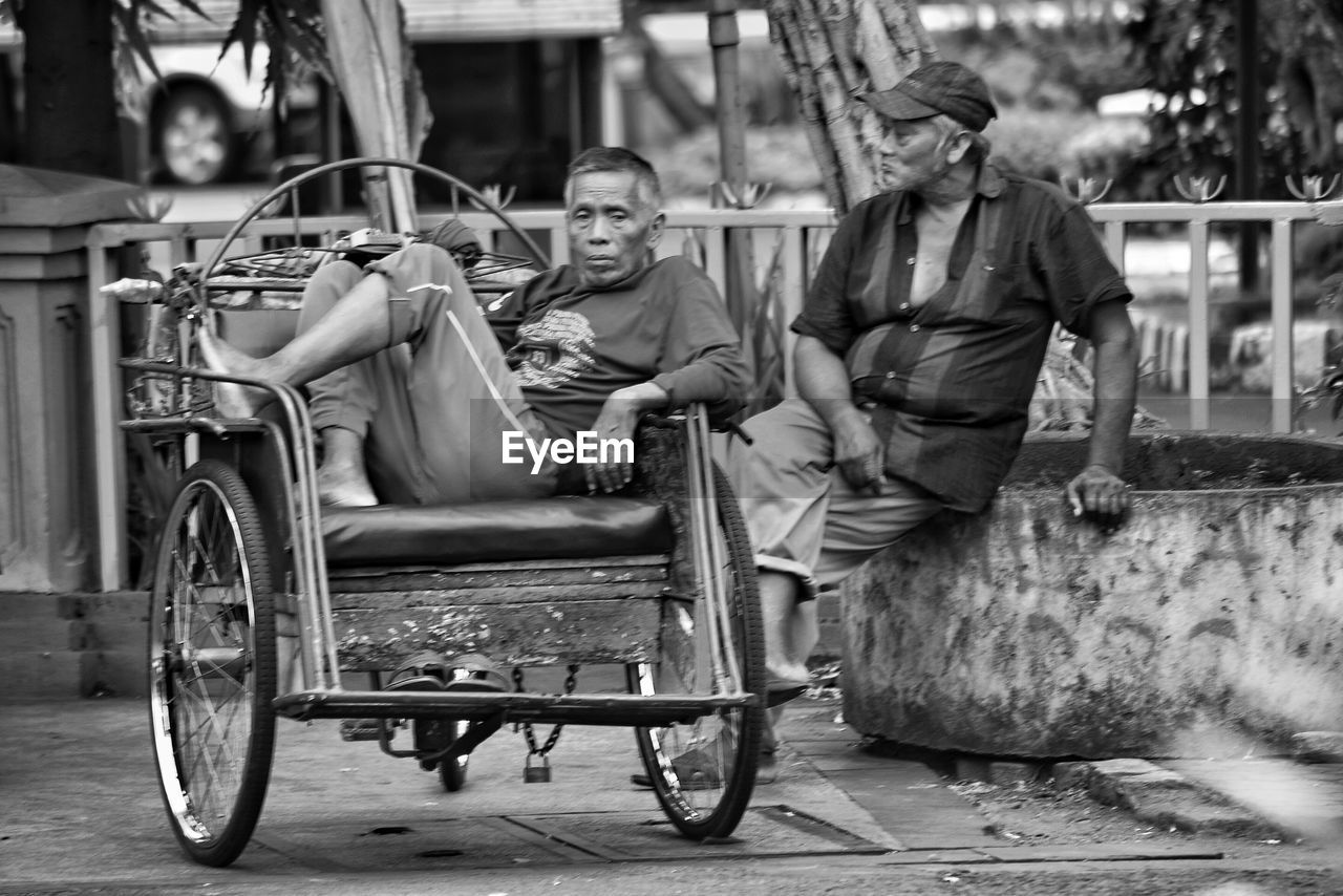 REAR VIEW OF MAN AND WOMAN SITTING ON RAILROAD TRACK