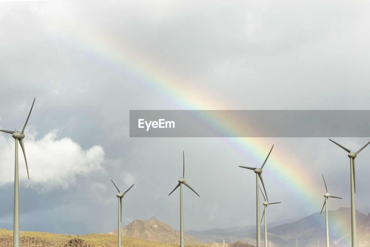 Scenic view of rainbow over windmills against cloudy sky