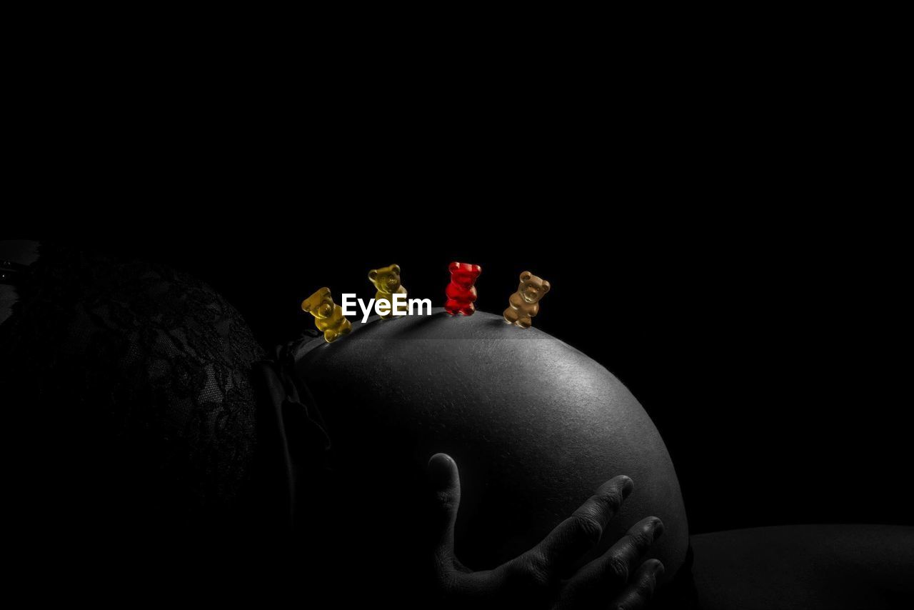 Side view of pregnant woman with gummi bears against black background