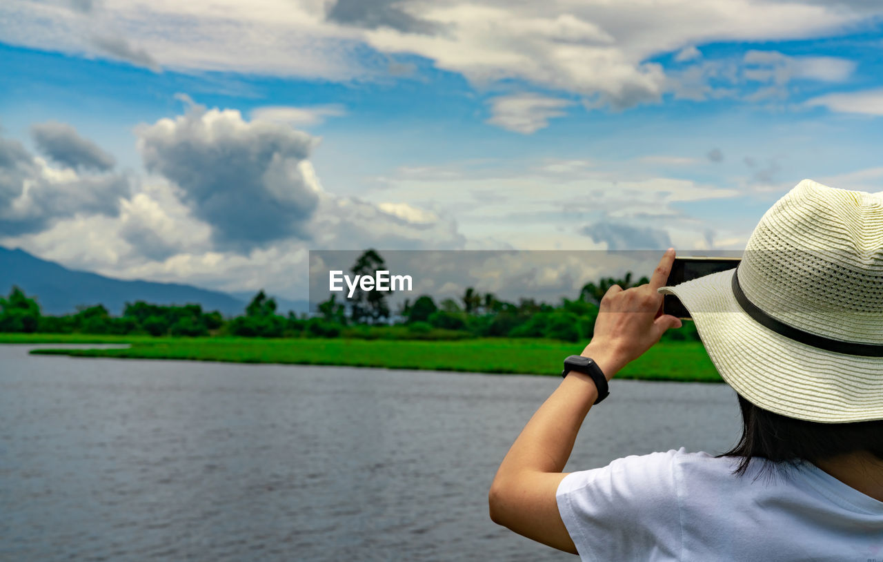 Asian woman use smartphone take a picture of beautiful landscape of river, mountain, and forest.