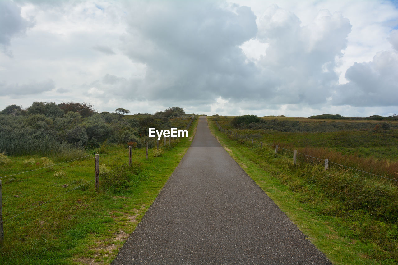 Empty road amidst field against sky. a way to the sea in the netherlands 