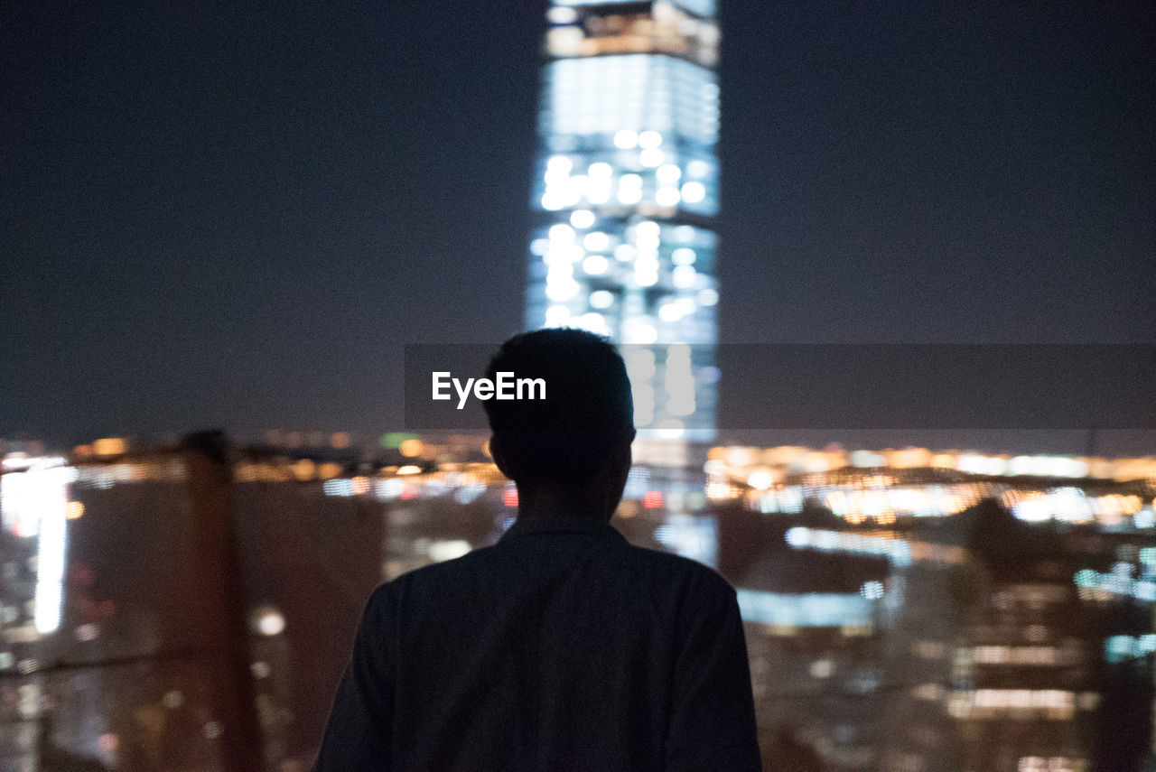 Rear view of man against illuminated residential district against sky at night