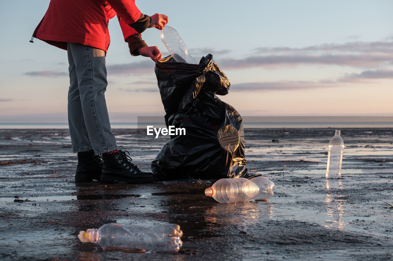 A woman cleans the bank of plastic bottles and puts the trash in a garbage bag