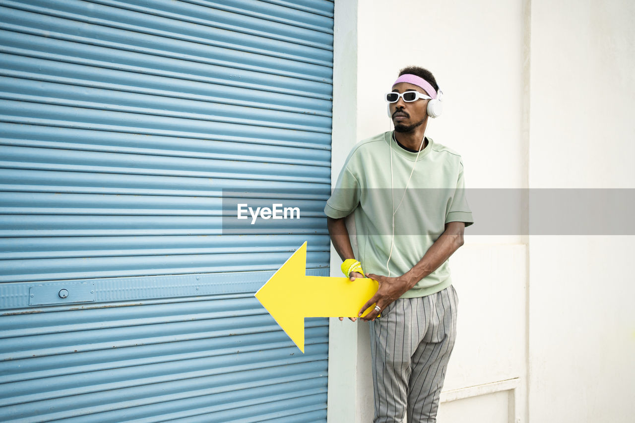 Man wearing sunglasses showing yellow arrow sign by blue shutter