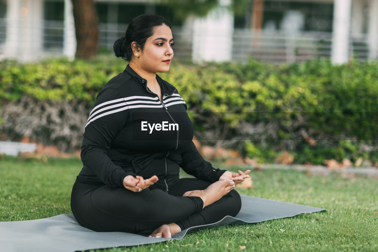 An indian woman practices yoga and meditation in the lotus asana pose in an outdoor summer park. 