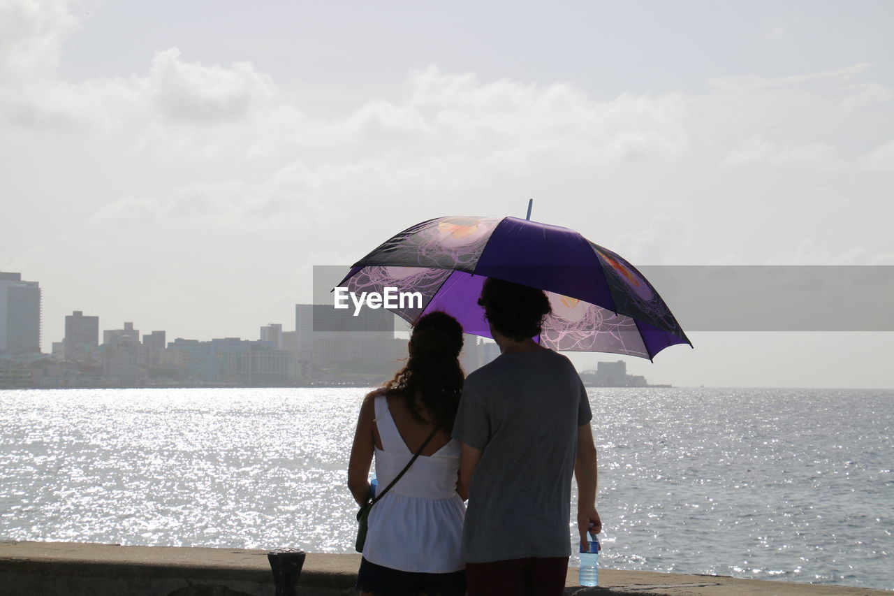 Rear view of couple with umbrella looking at city and sea