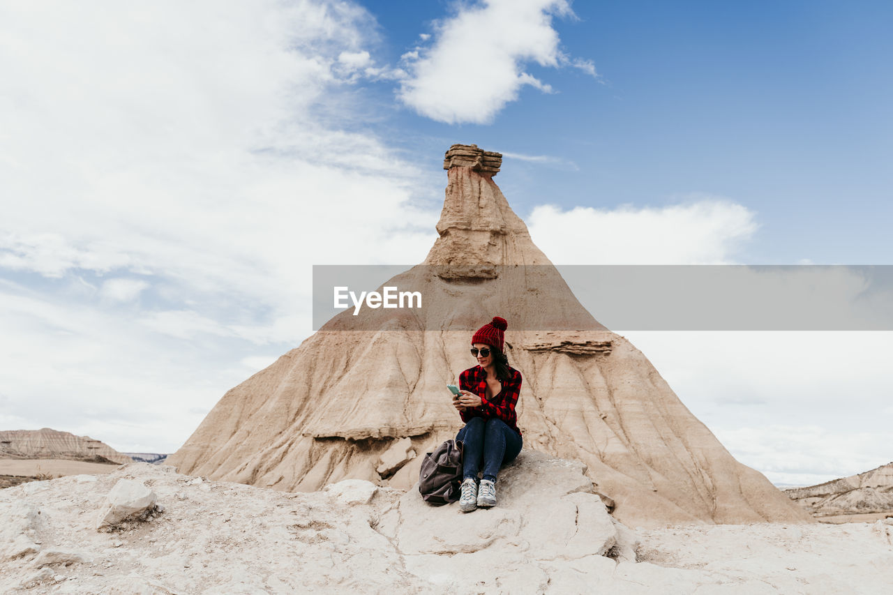 Spain, navarre, female tourist using smart phone in front of sandstone rock formation in bardenas reales