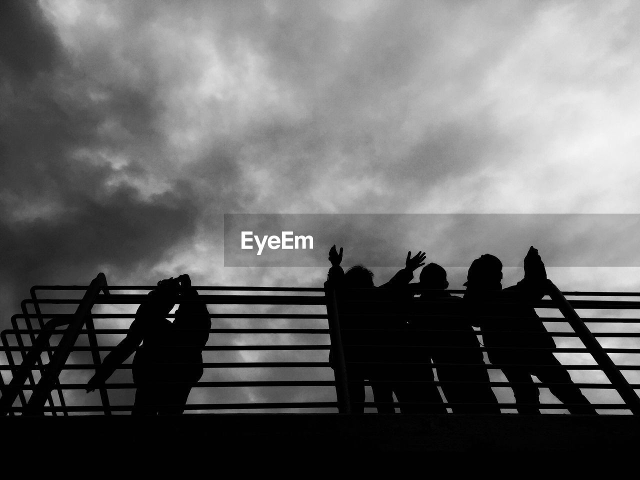 Silhouette people on bridge against cloudy sky