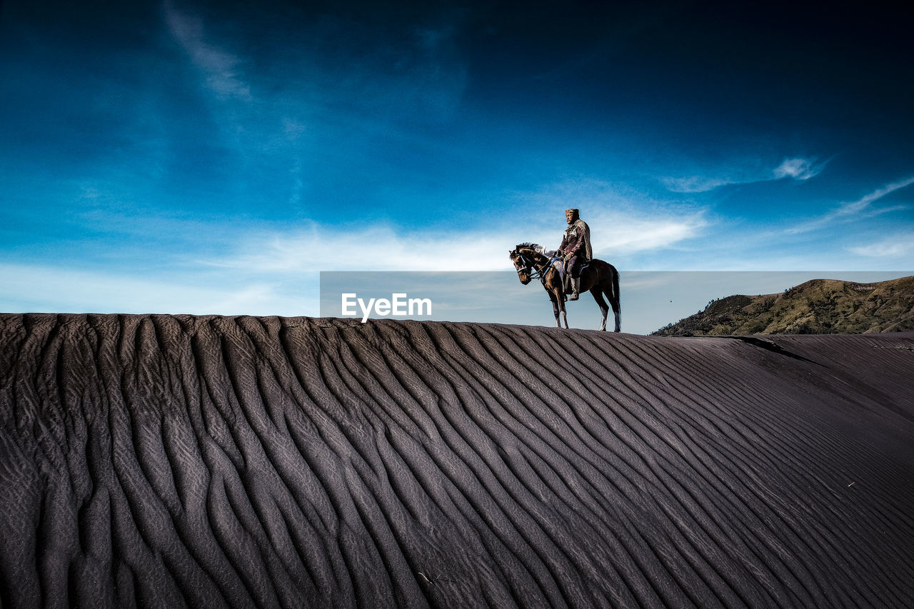 Mid adult man riding horse on sand at desert against sky