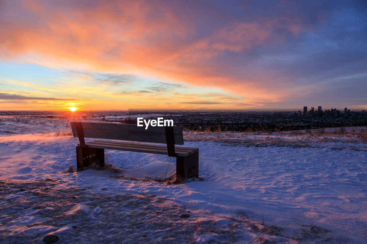 Empty bench in a snowy landscape at sunrise
