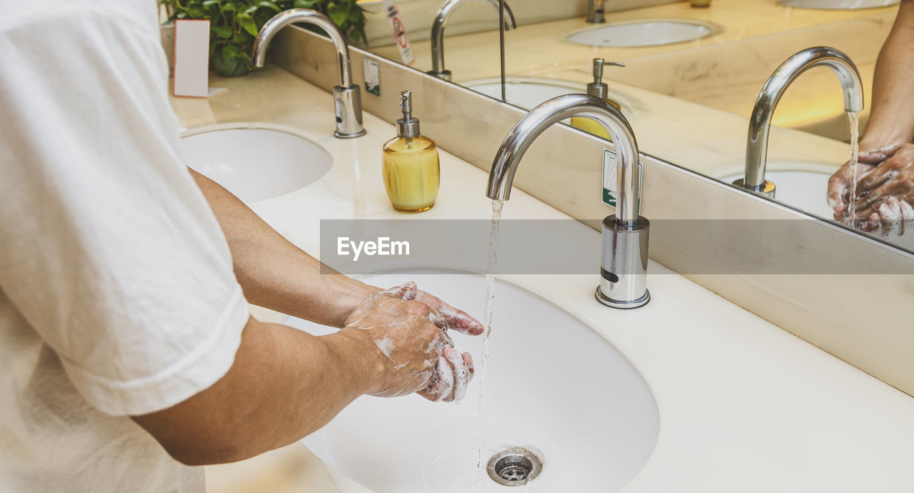 Closeup hands washing with chrome faucet and soap for coronavirus pandemic prevention in bathroom,