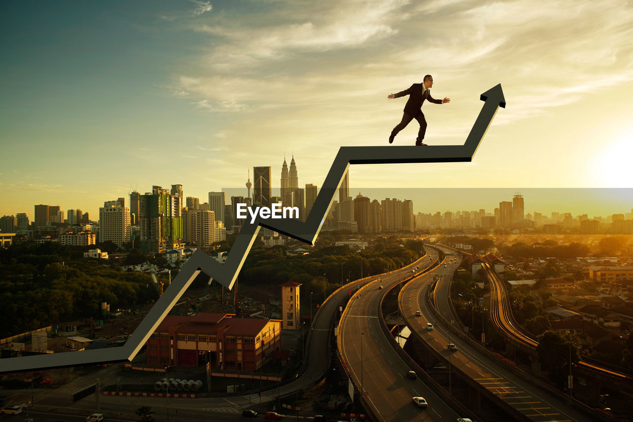 Low angle view of businessman standing on arrow symbol in city during sunset