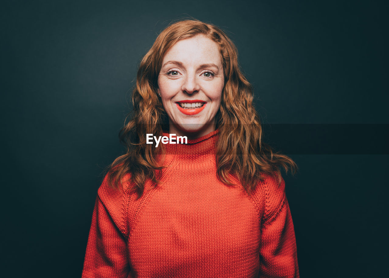 Portrait of smiling woman in orange top against gray background