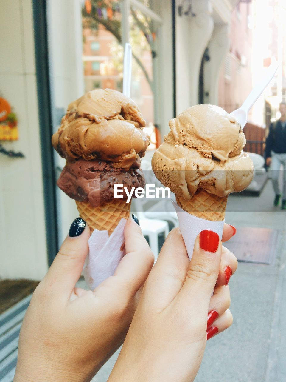 Cropped hands of friends holding ice cream cones on sidewalk