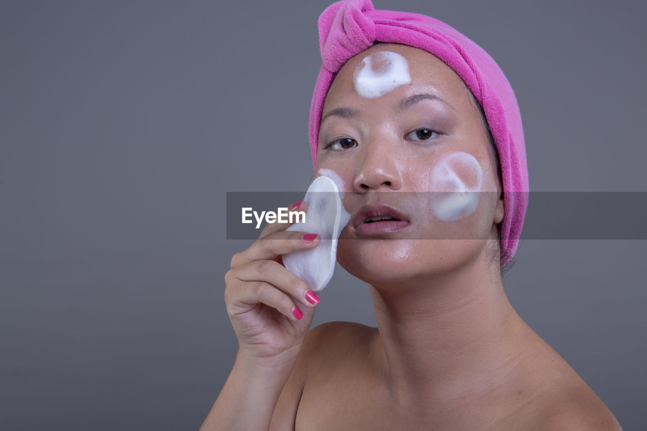 body care, portrait, human face, studio shot, women, adult, headshot, one person, indoors, skin care, young adult, pink, beauty treatment, human head, make-up, skin, beauty product, wellbeing, applying, nose, female, gray, gray background, human skin, lifestyles, facial mask - beauty product, hygiene, close-up, relaxation, beauty spa, healthcare and medicine, front view, hand, colored background, cut out, body care and beauty, looking at camera, copy space