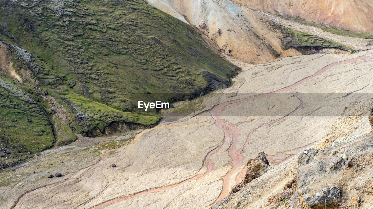 Pink creek is flowing down iceland's mossy highlands on a sunny day