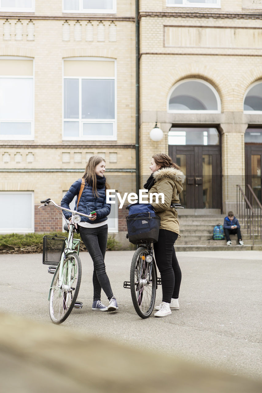 Schoolgirls with bicycles communicating outside school building