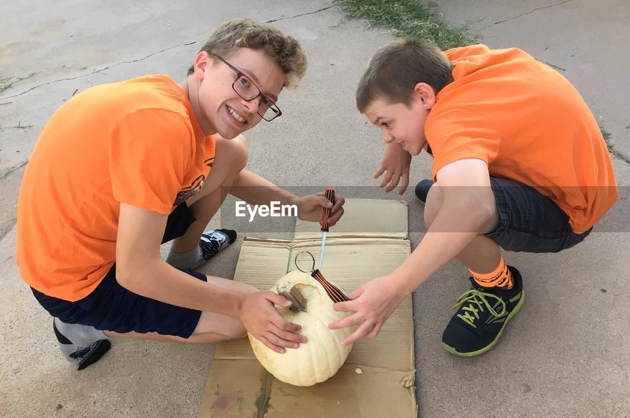 Two boys wearing orange shirts getting ready to carve a white pumpkin on halloween