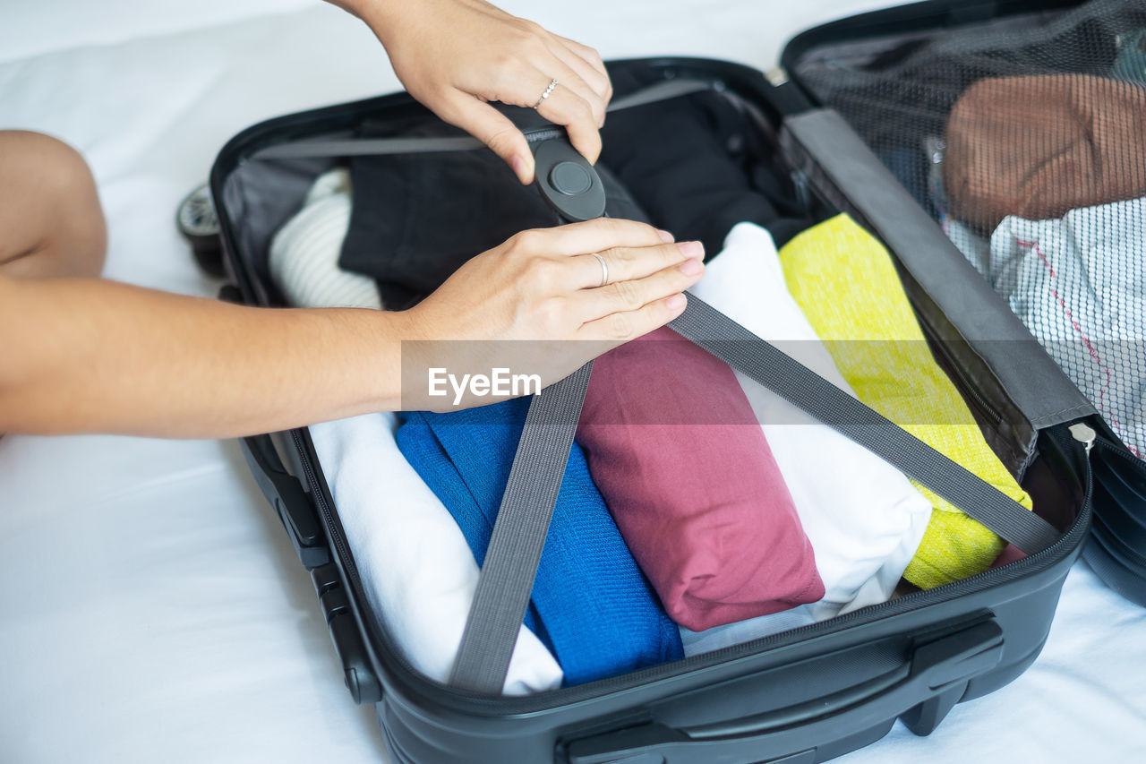 Cropped hands of woman packing luggage on bed
