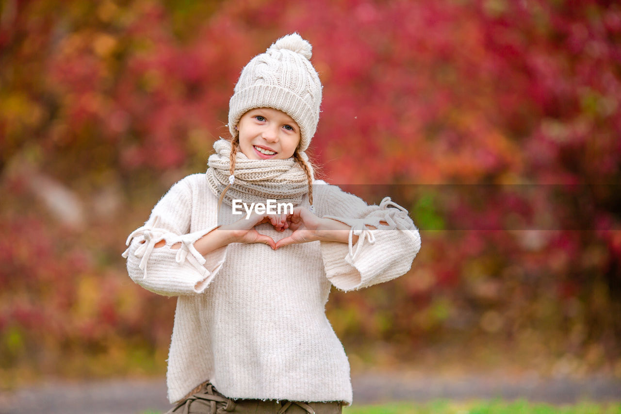 PORTRAIT OF SMILING GIRL STANDING AGAINST TREE