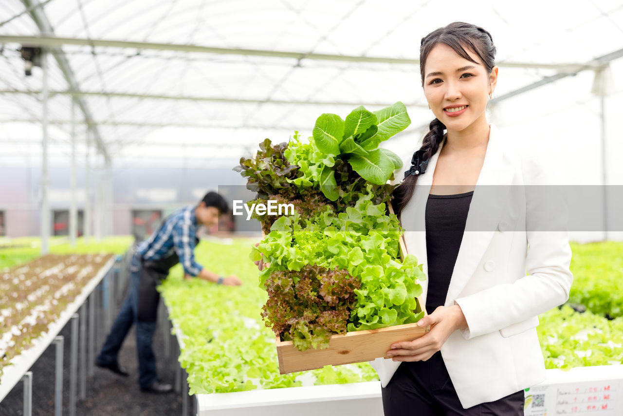 Portrait of a smiling young woman standing in greenhouse