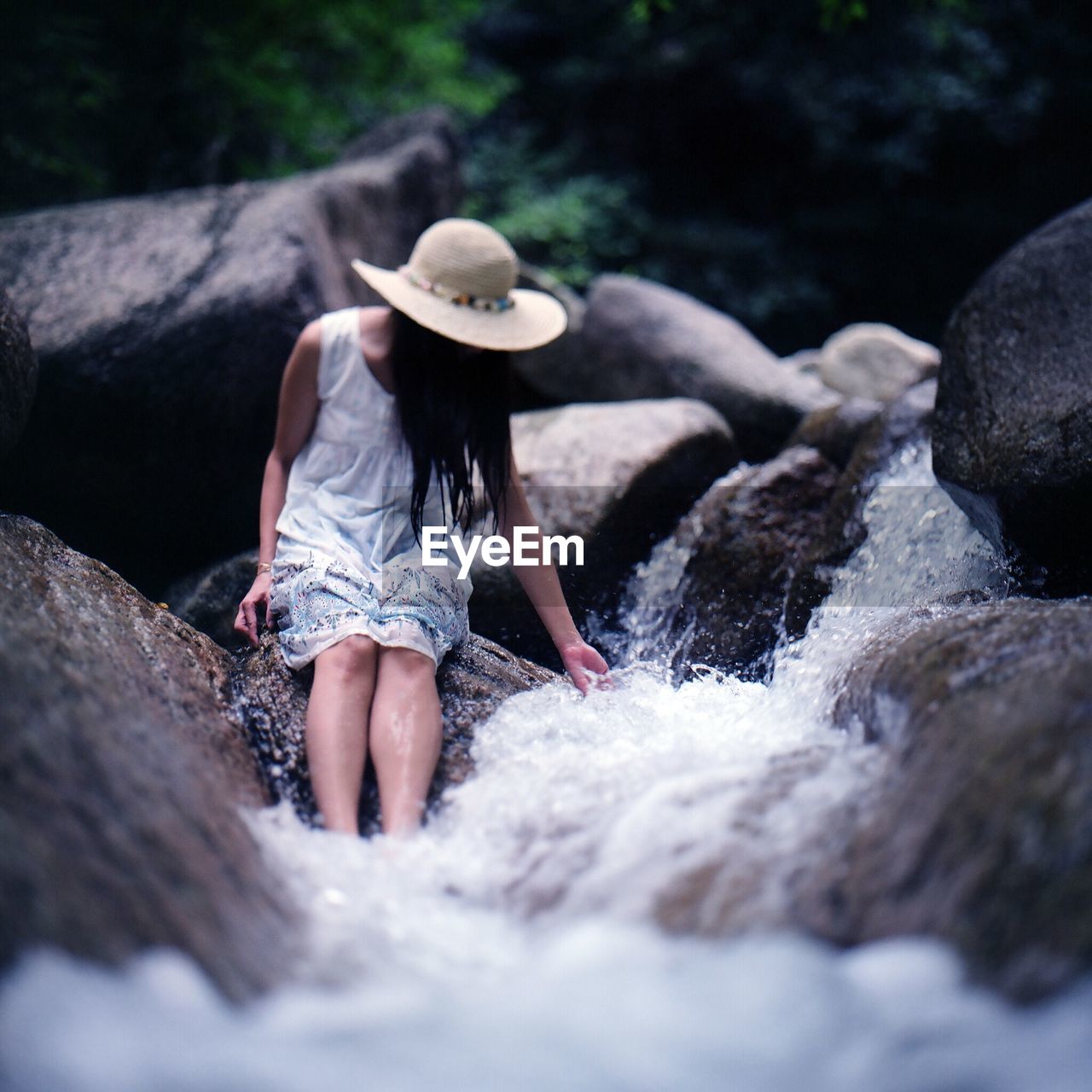 Woman sitting on rock in stream