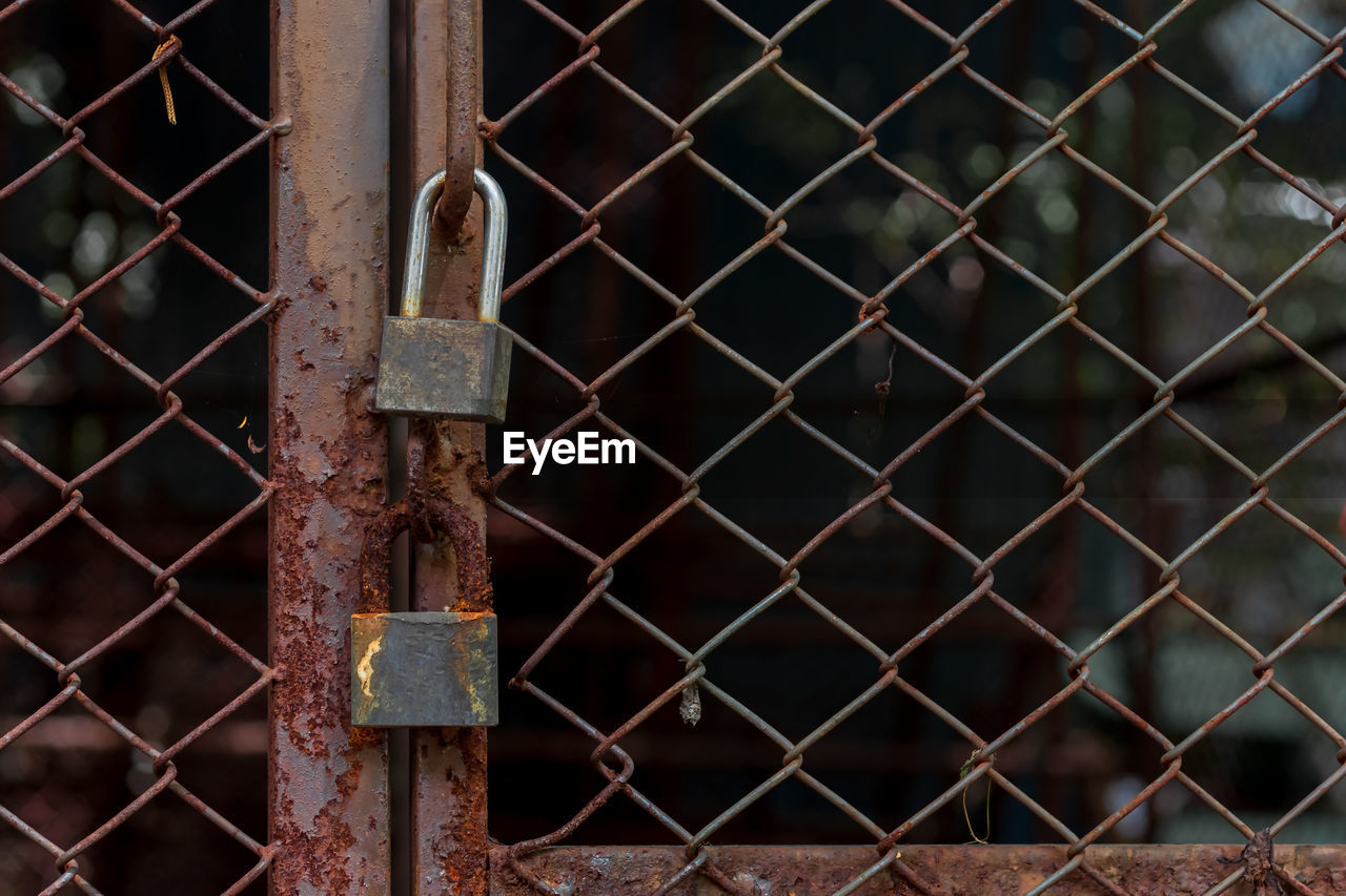 Abandoned padlocks locked on rusty wire mesh steel door background.