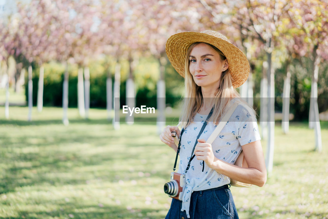 Portrait of a woman in a hat with a camera in the cherry blossoms park. copy space. travel concept.