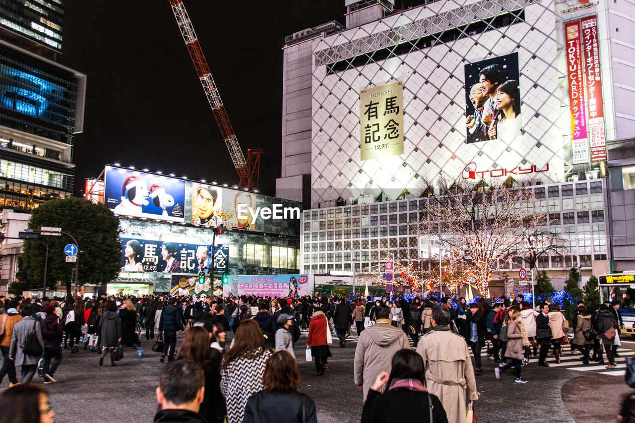 CROWD OF PEOPLE WALKING ON ILLUMINATED STREET