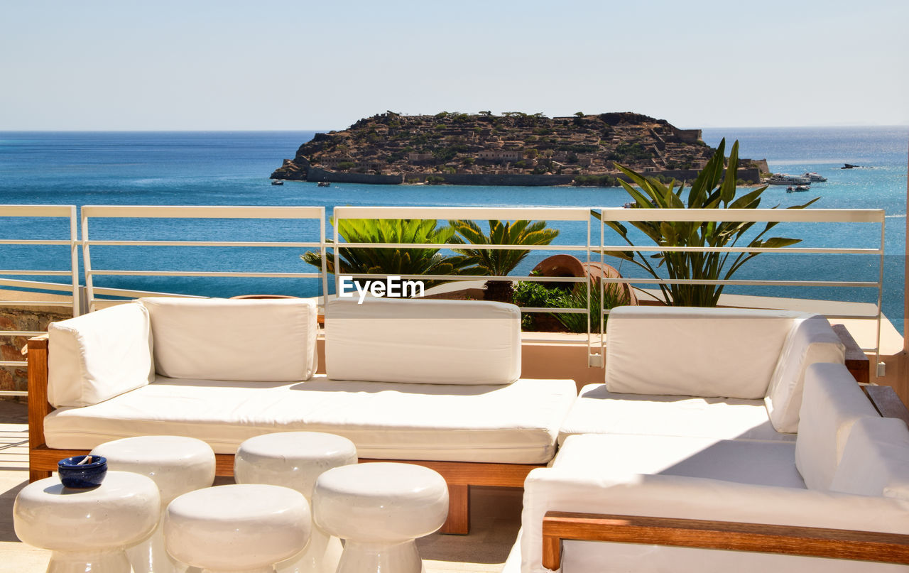 Empty sofa by sea against clear sky