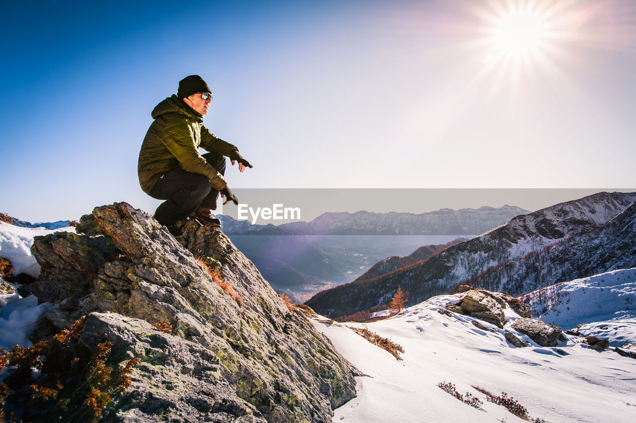Man crouching on snowcapped mountain against sky