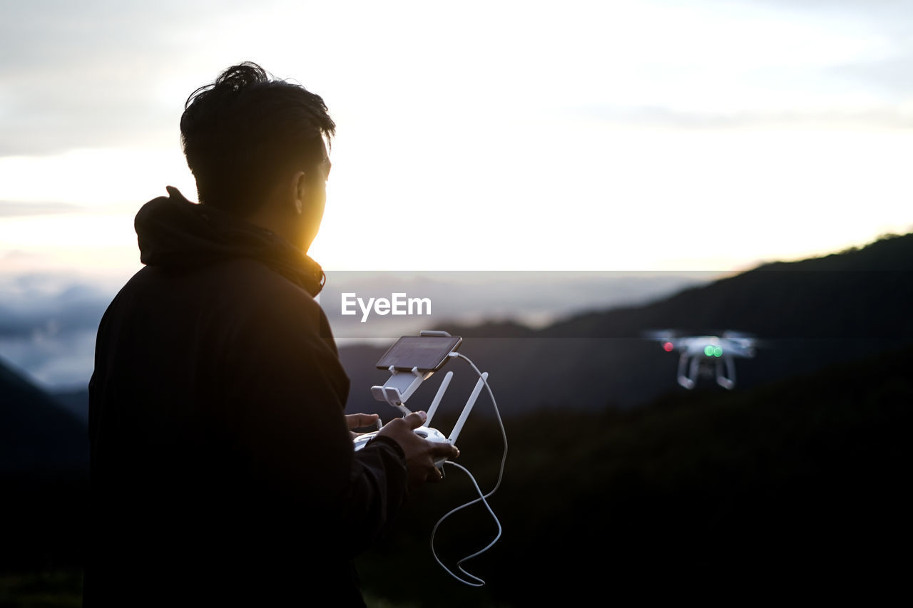 Side view of man flying drone over mountain against sky during sunset