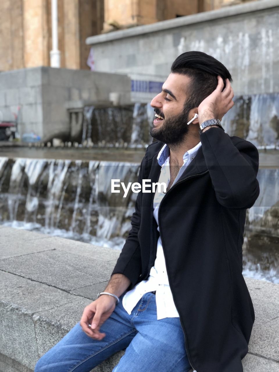 Smiling man with hand in hair sitting outdoors