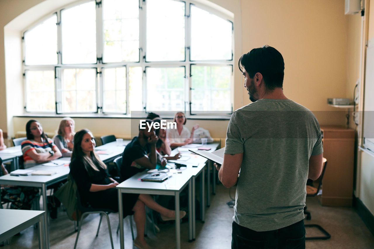 Rear view of male teacher standing while teaching students in classroom