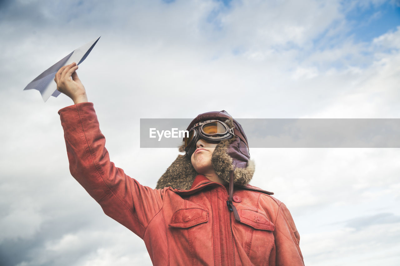 Boy playing with paper airplane against cloudy sky