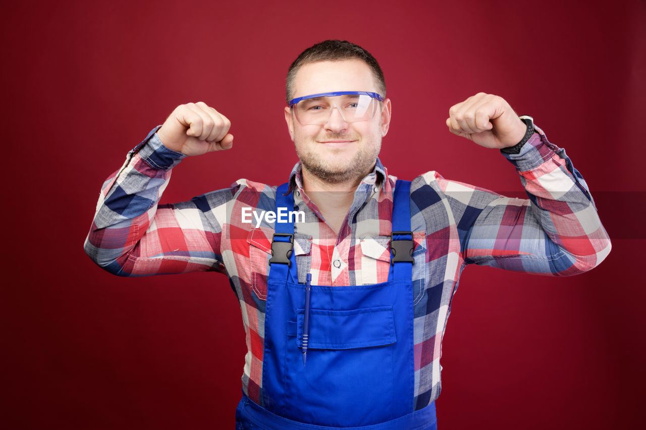 PORTRAIT OF YOUNG MAN STANDING AGAINST GRAY BACKGROUND